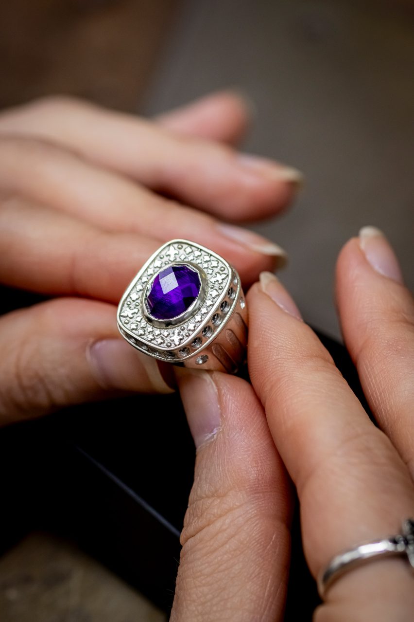 A photograph of a person holding a silver ring with a purple jewel in its centre.