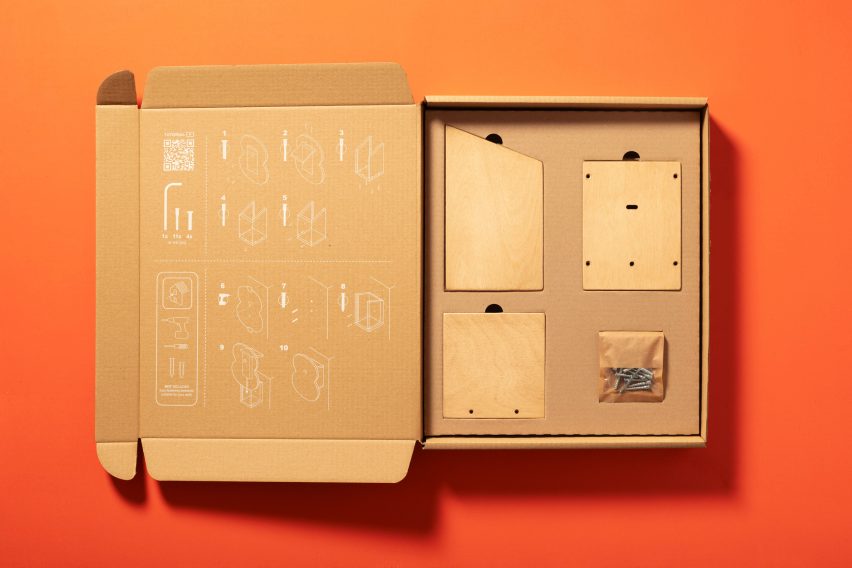 A photograph of an open cardboard box with pieces of wood inside, laid flat against an orange background.