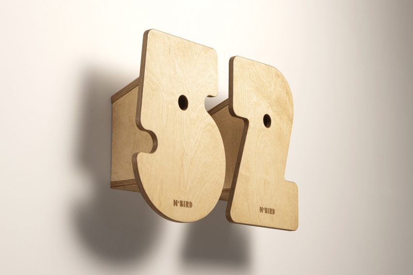 A photograph of two wooden bird boxes on a white wall, adjacent to one another. One is shaped as the number five and the other shaped as the number two.