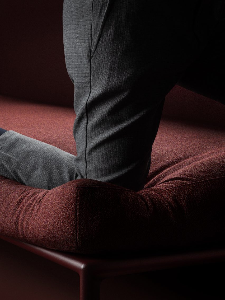 Close-up photo of a person kneeling on a dark burgundy sofa seat, with their knee sinking deep into the cushion