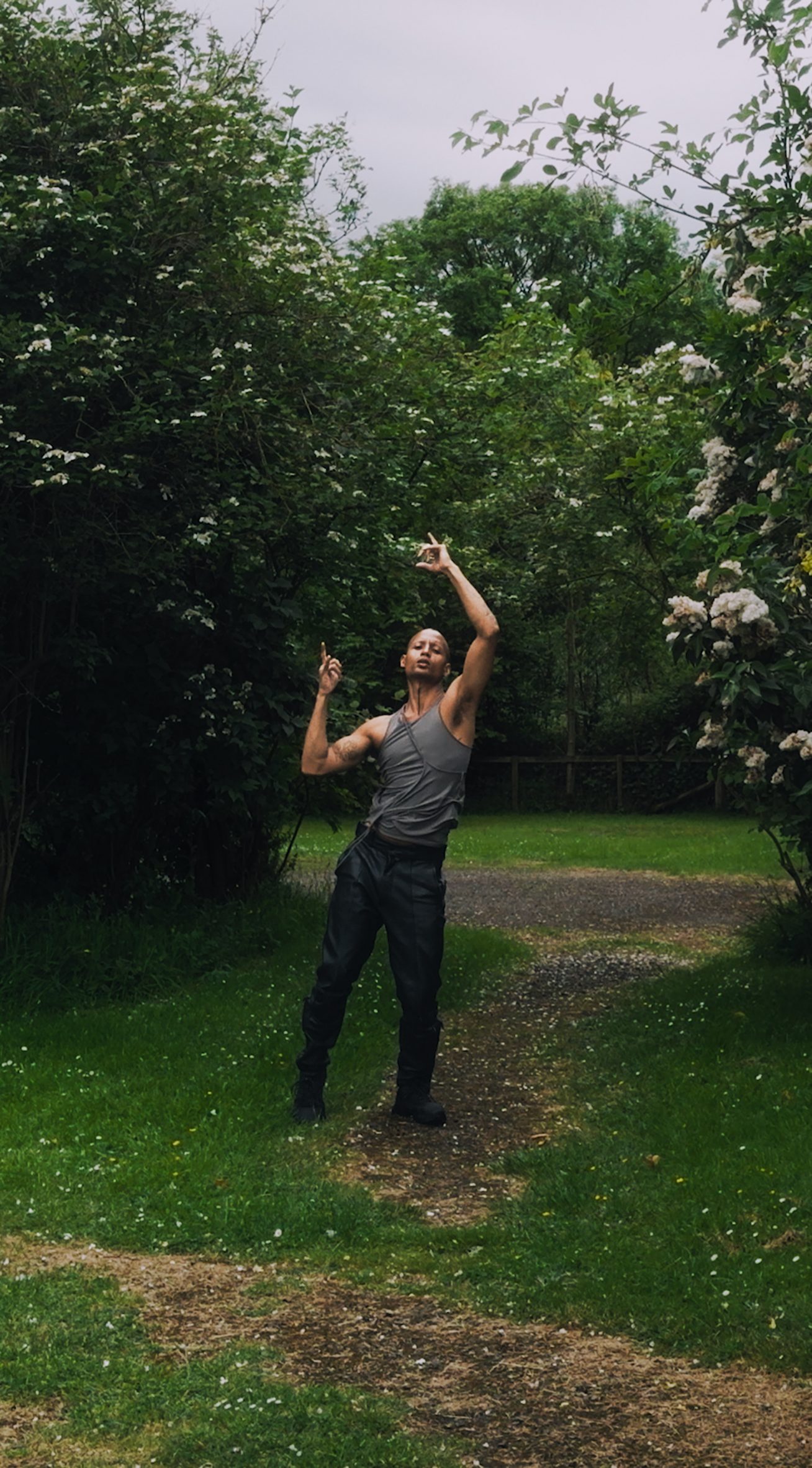 A photograph of a person in grey and black clothing, amongst an outdoor environment of green trees and grass.