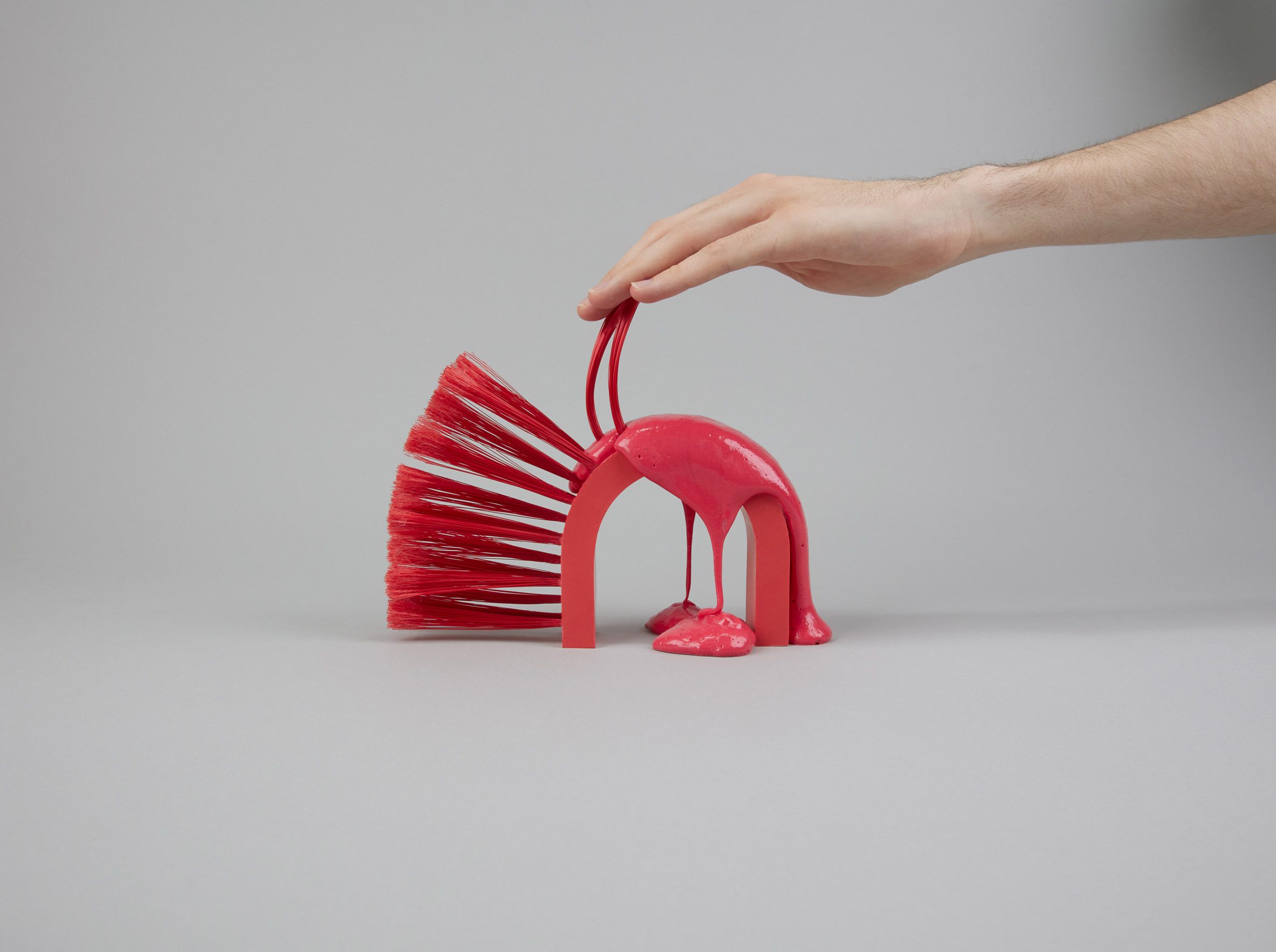 A photograph of a person's hand interacting with a handle attached to a red object, against a grey background.