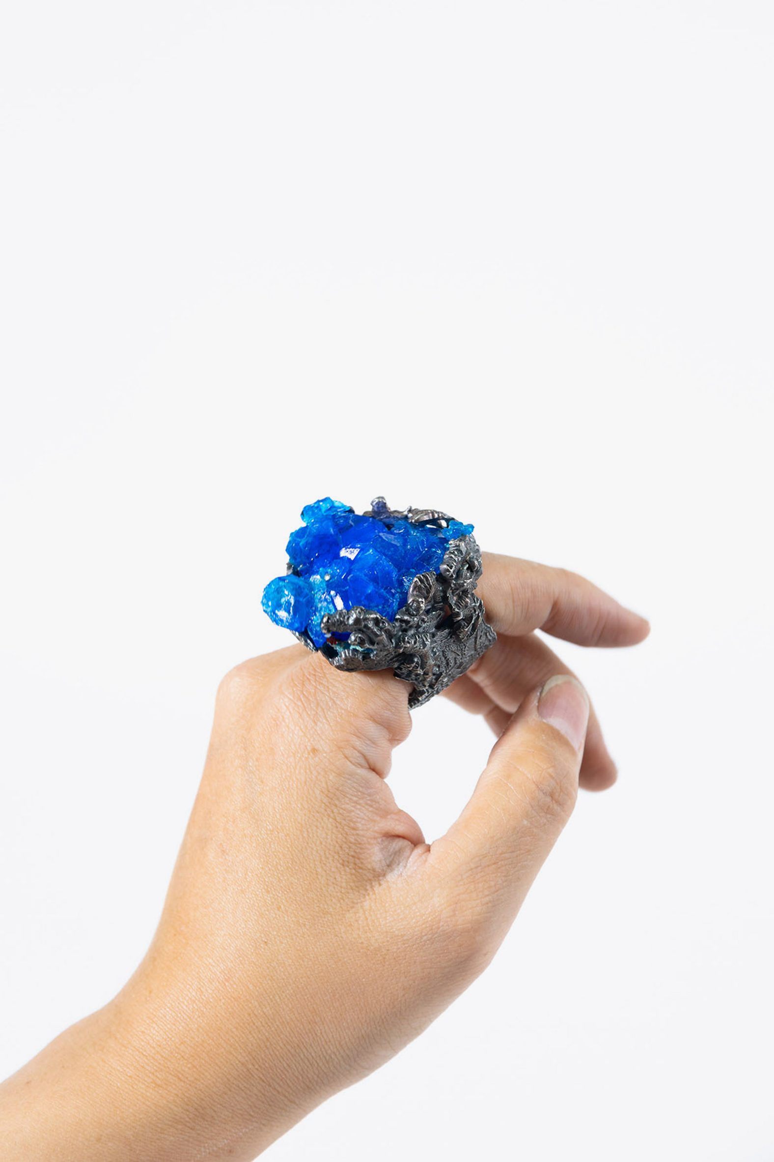 A photograph of a person's hand wearing a large blue and grey ring, against a white background.