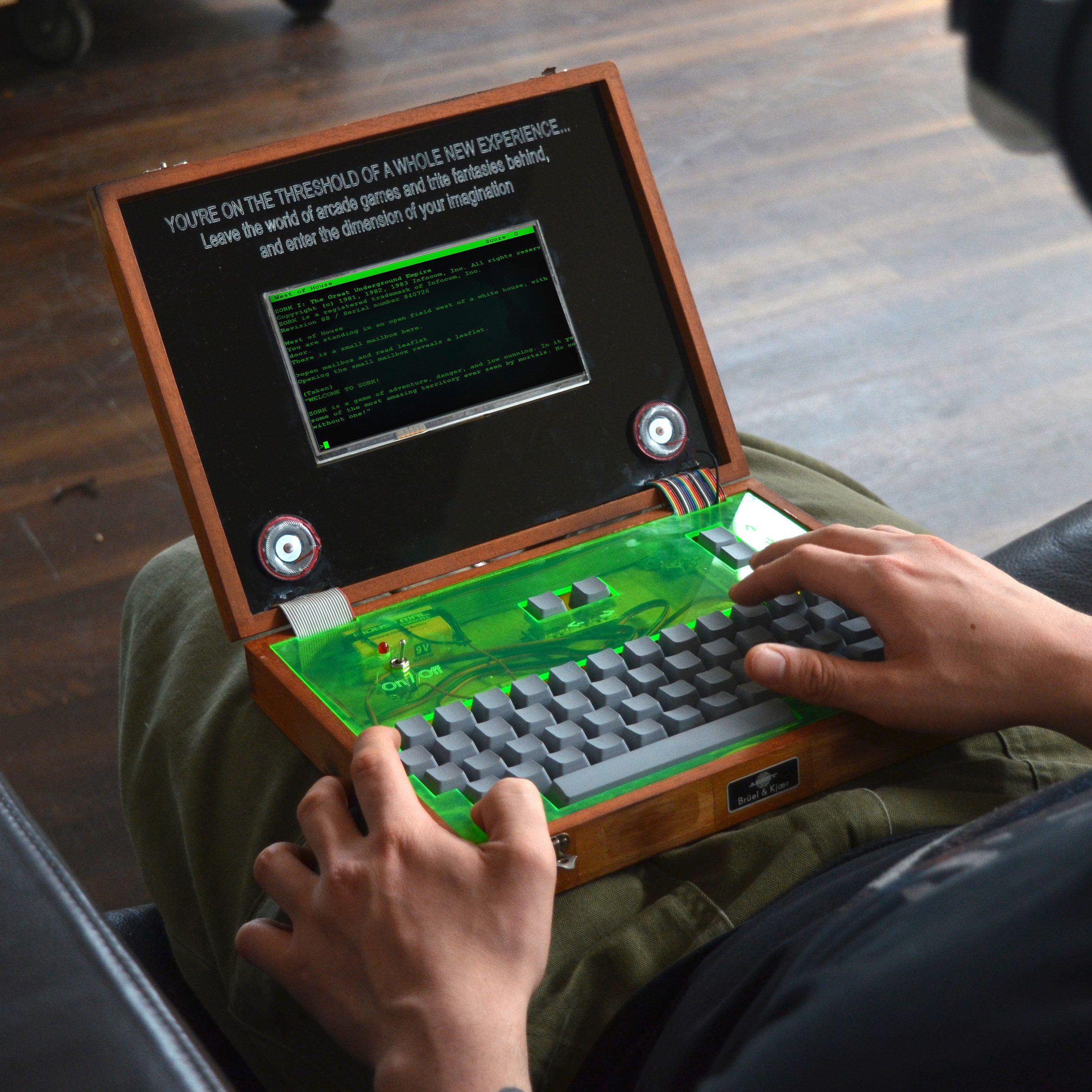 A photograph of a person on a laptop with a green keyboard and a black screen on display. 