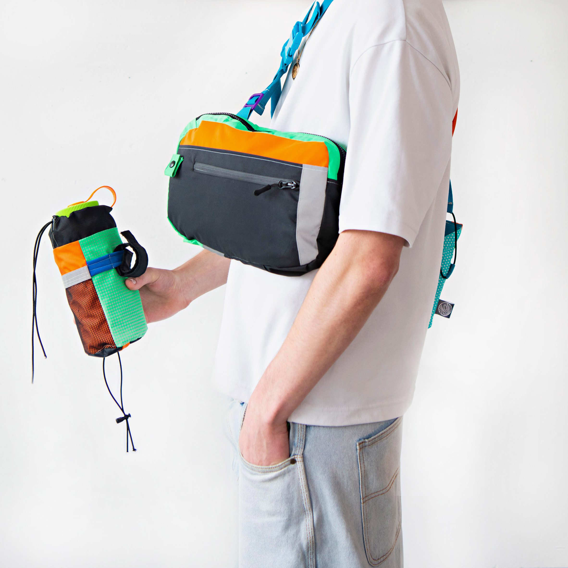 A photograph of a person wearing a bag in tones of grey, orange, green and blue, holding a water bottle case in the same colours.