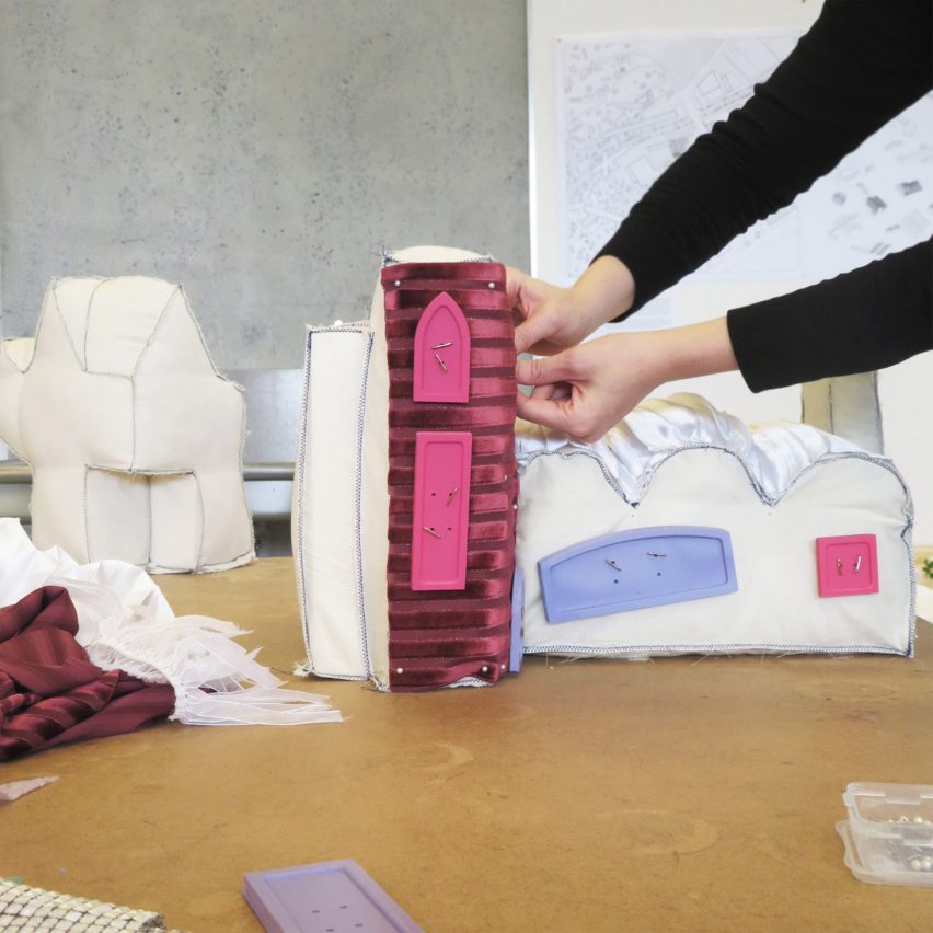 A photograph of a person handling an architectural model made of fabric, in colours of pink, purple and white.