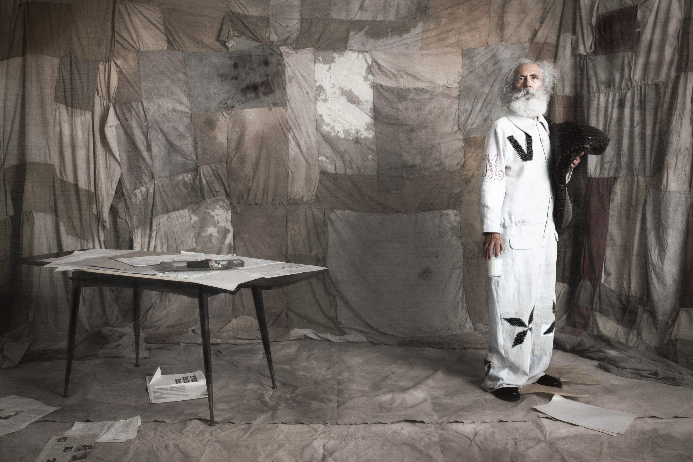 A photograph of a person wearing white in a grey space, adjacent to a table.