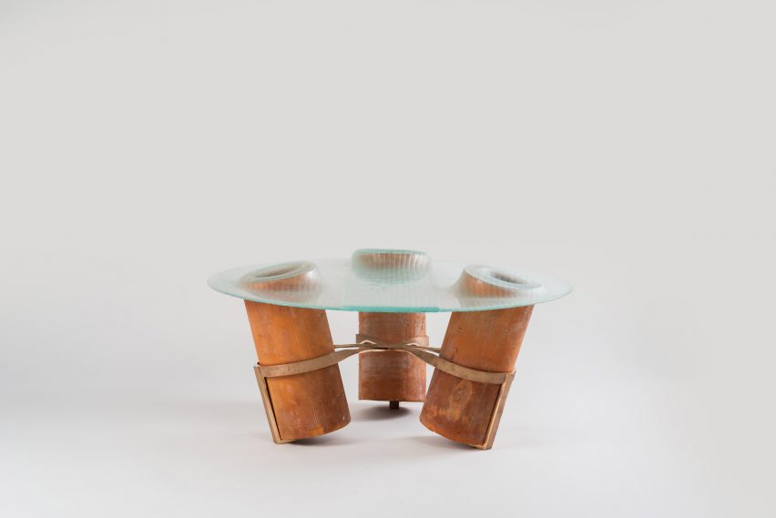 A photograph of a table with a transparent tabletop and three copper-coloured legs.
