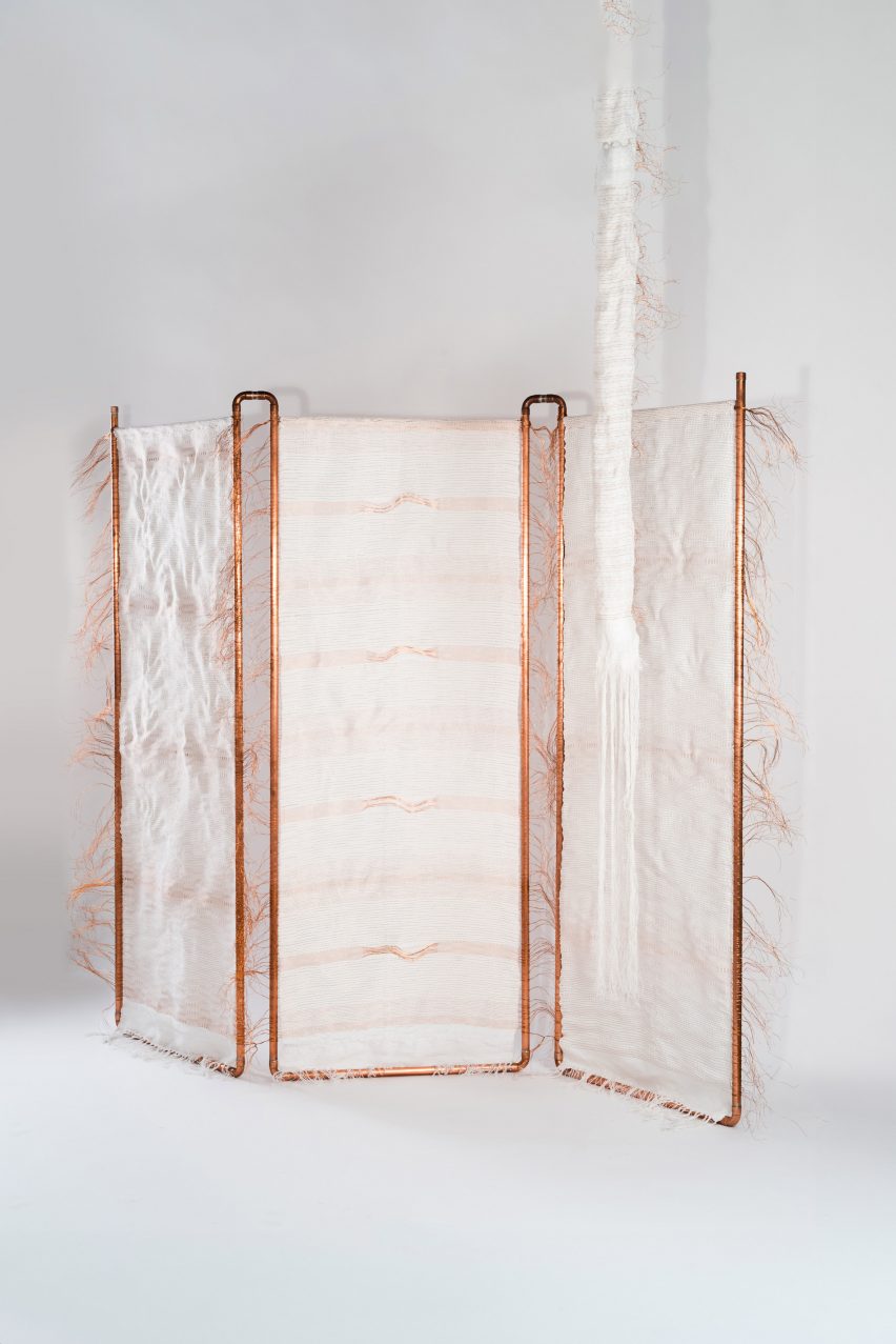 A photograph of a dressing screen made of white fabric and a copper wire frame, against a white background.