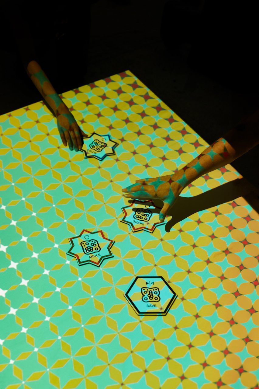 A photograph of two people interacting with star and hexagonal-shaped cards on a green and yellow patterned surface.
