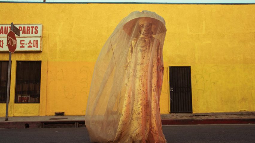 Photo of person wearing a hat and veil in front of a yellow wall