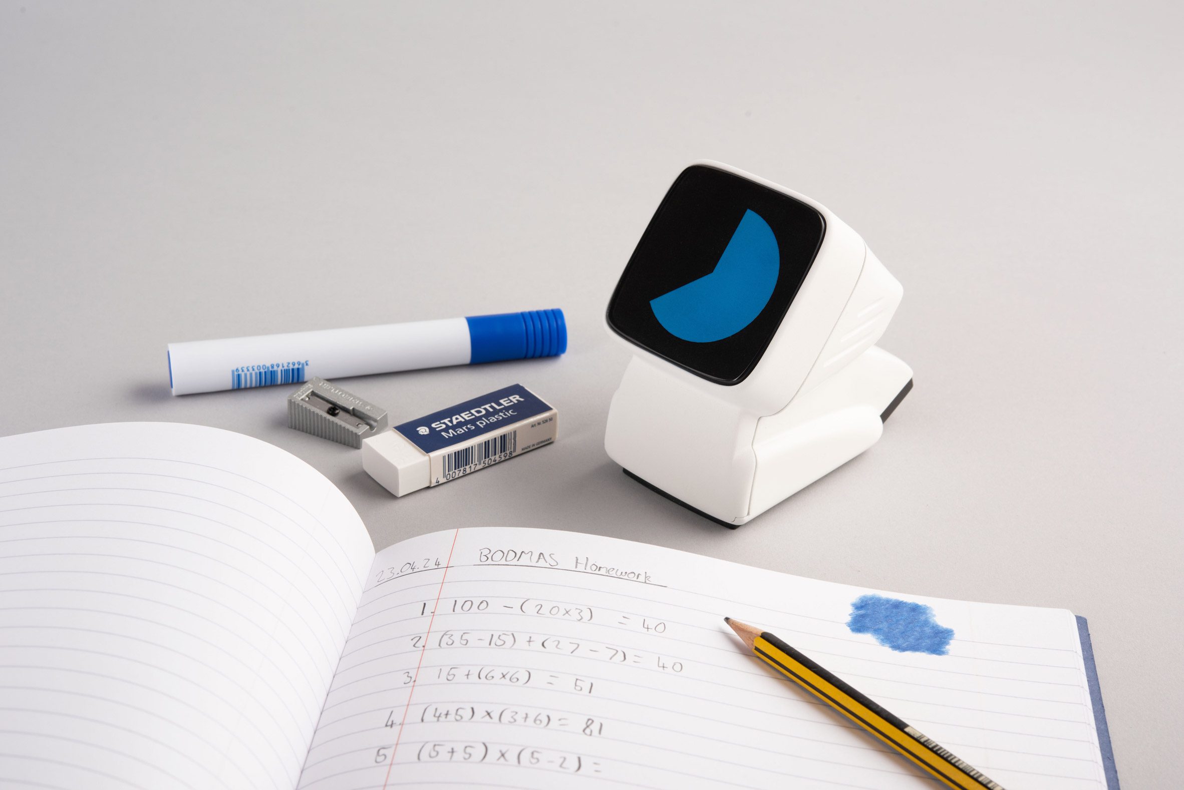 A photograph of a notebook open on a page surrounded with stationary and an electronic device in tones of white, black and blue.