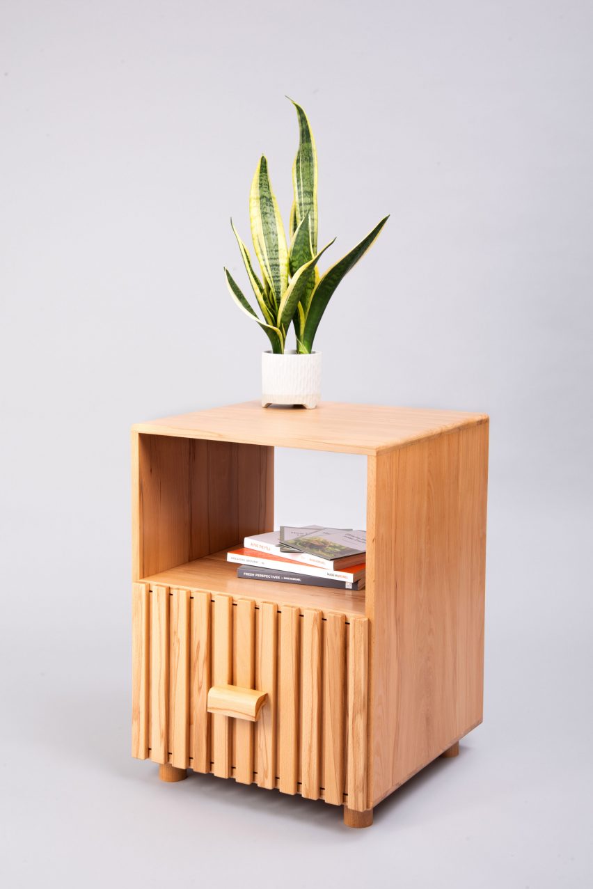 A photograph of a brown wooden table with a houseplant on top, against a grey backdrop.