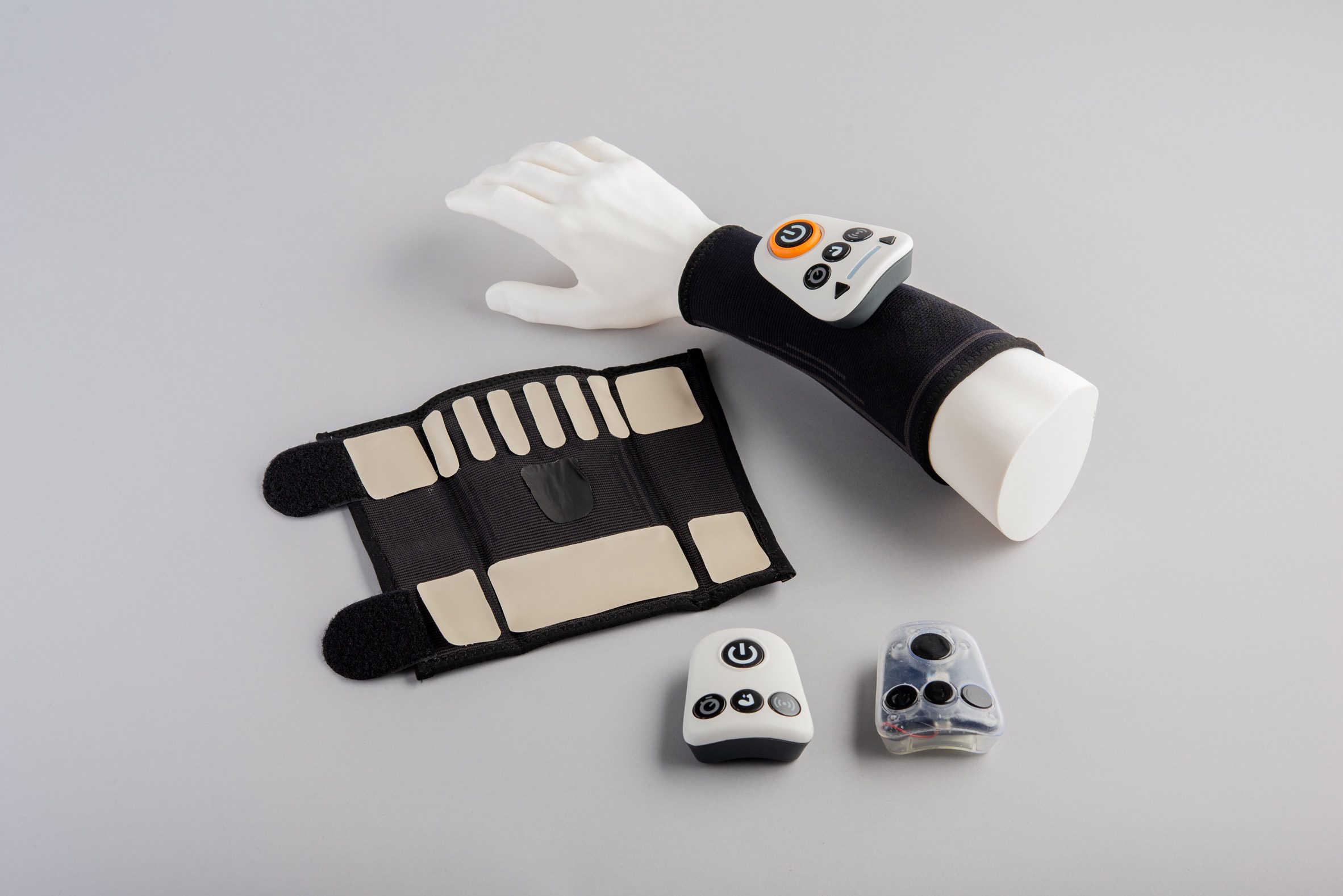 A photograph of a hand mannequin with a black band and gadget on it; with the same objects placed next to it against a grey backdrop.