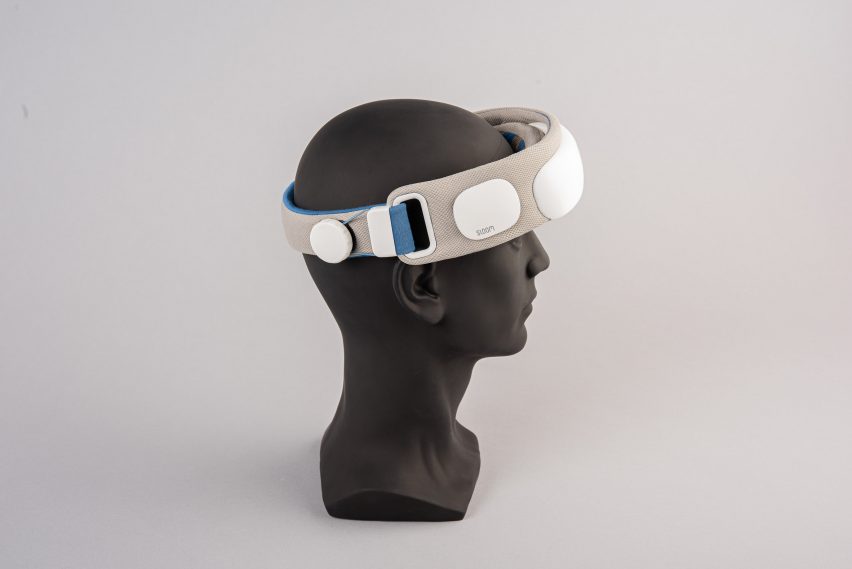 A photograph of a black mannequin head with a device in tones of grey, white and blue wrapped around it. 