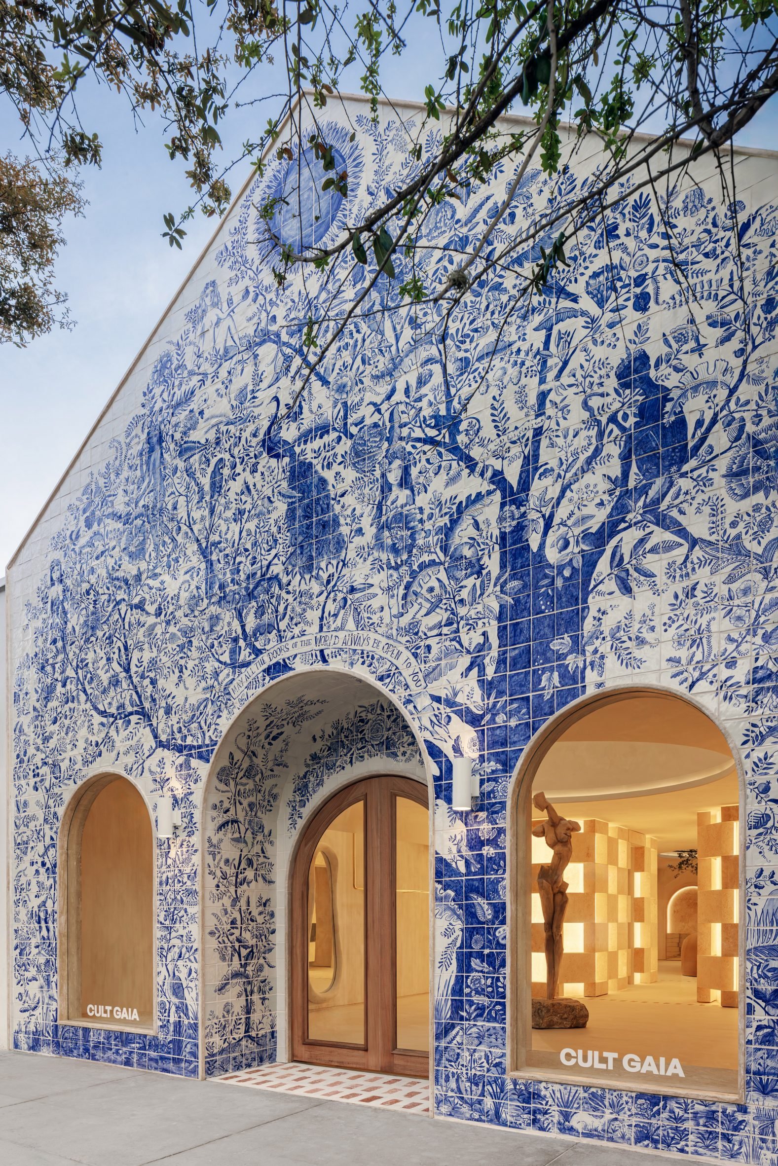 Blue tree of life mural painted across a tiled facade, viewed from an angle