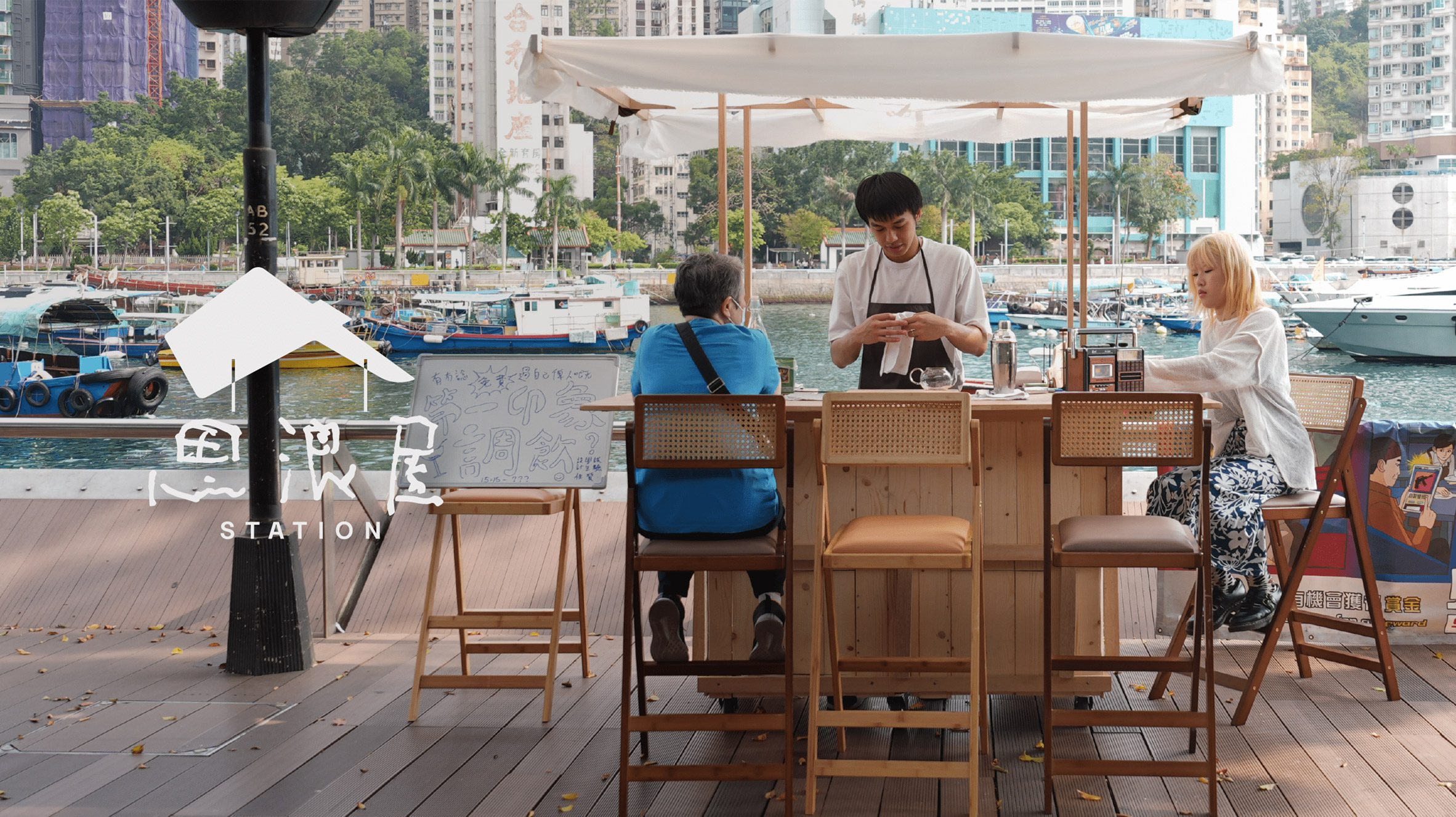 A photograph of people sat around an outside wooden bar by a dock