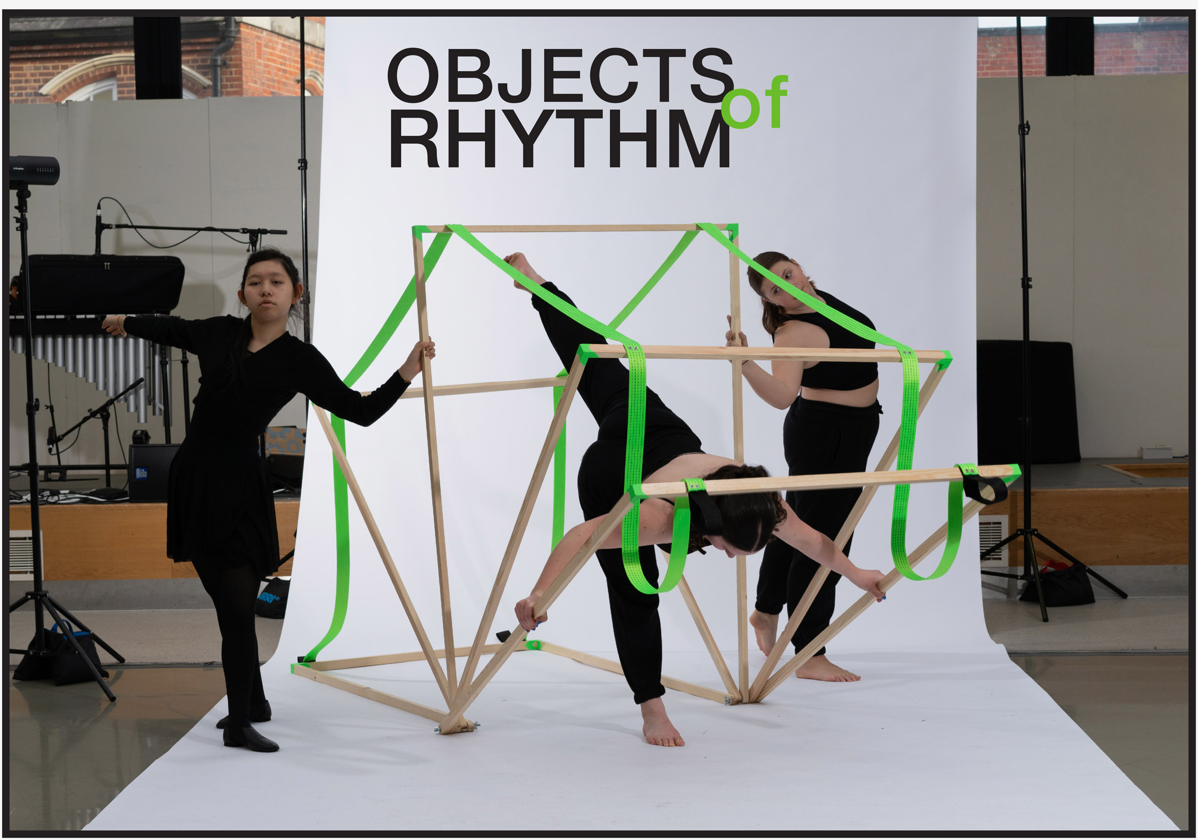 A photograph of three people dressed in black handing a wooden structure with green rope around it. In the centre of the image, above the people, are the words 'objects of rhythm' written in black and green. 