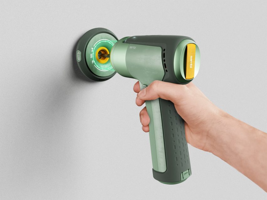 A photograph of person's hand holding a green drill to a white wall.