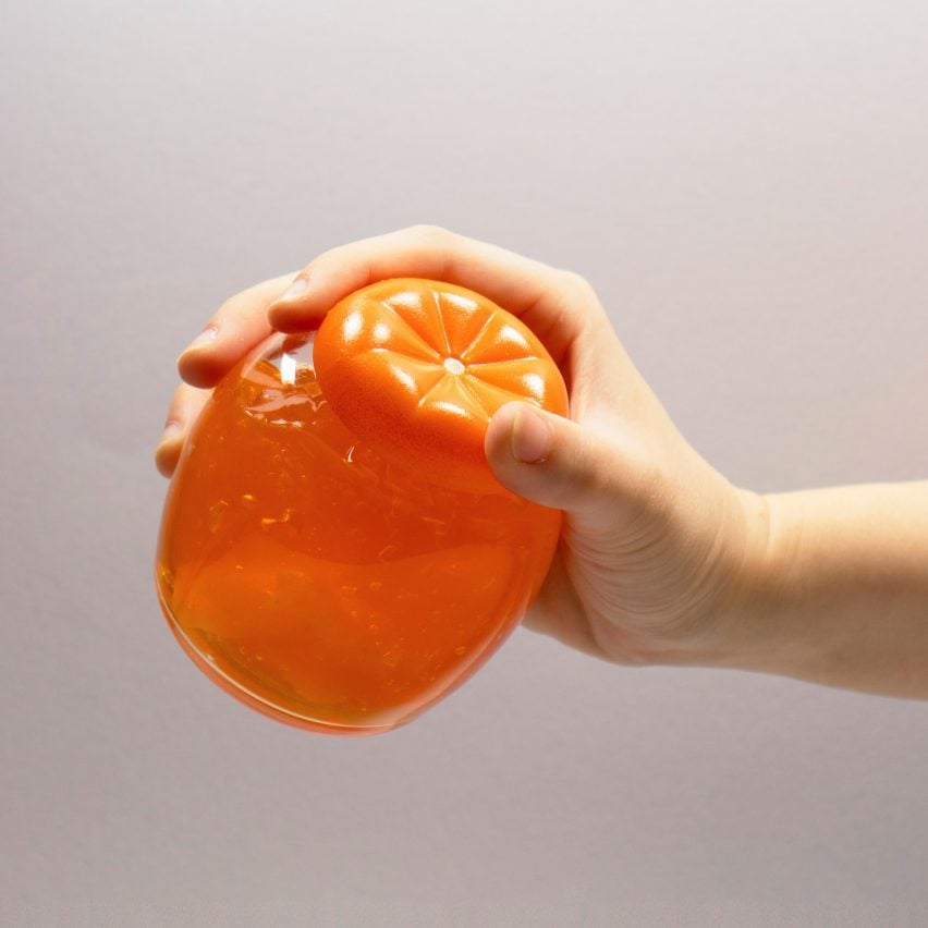 A photograph of a person's hand holding an orange coloured circular object against a white background.