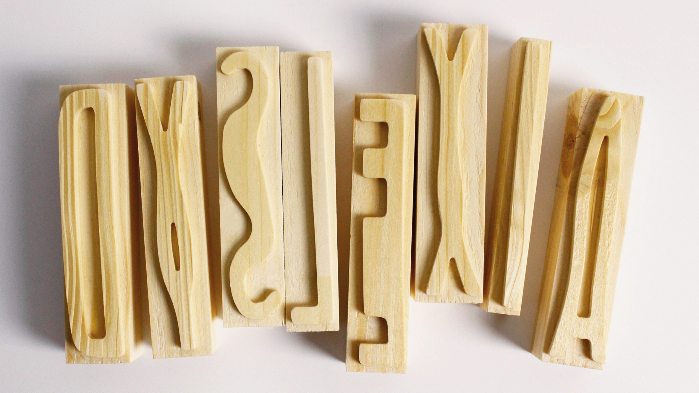 A photograph of wooden letterpress blocks displaying various characters from a custom typeface 