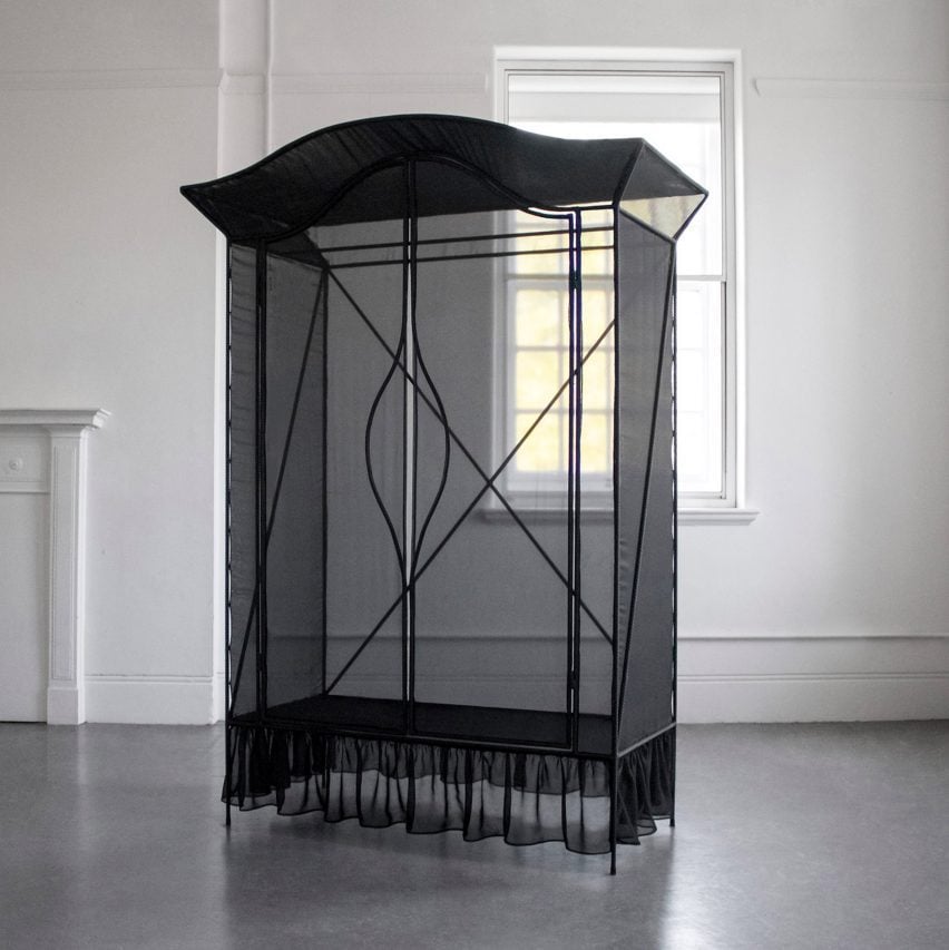 A photograph of a black wardrobe frame covered in black netting in a white room