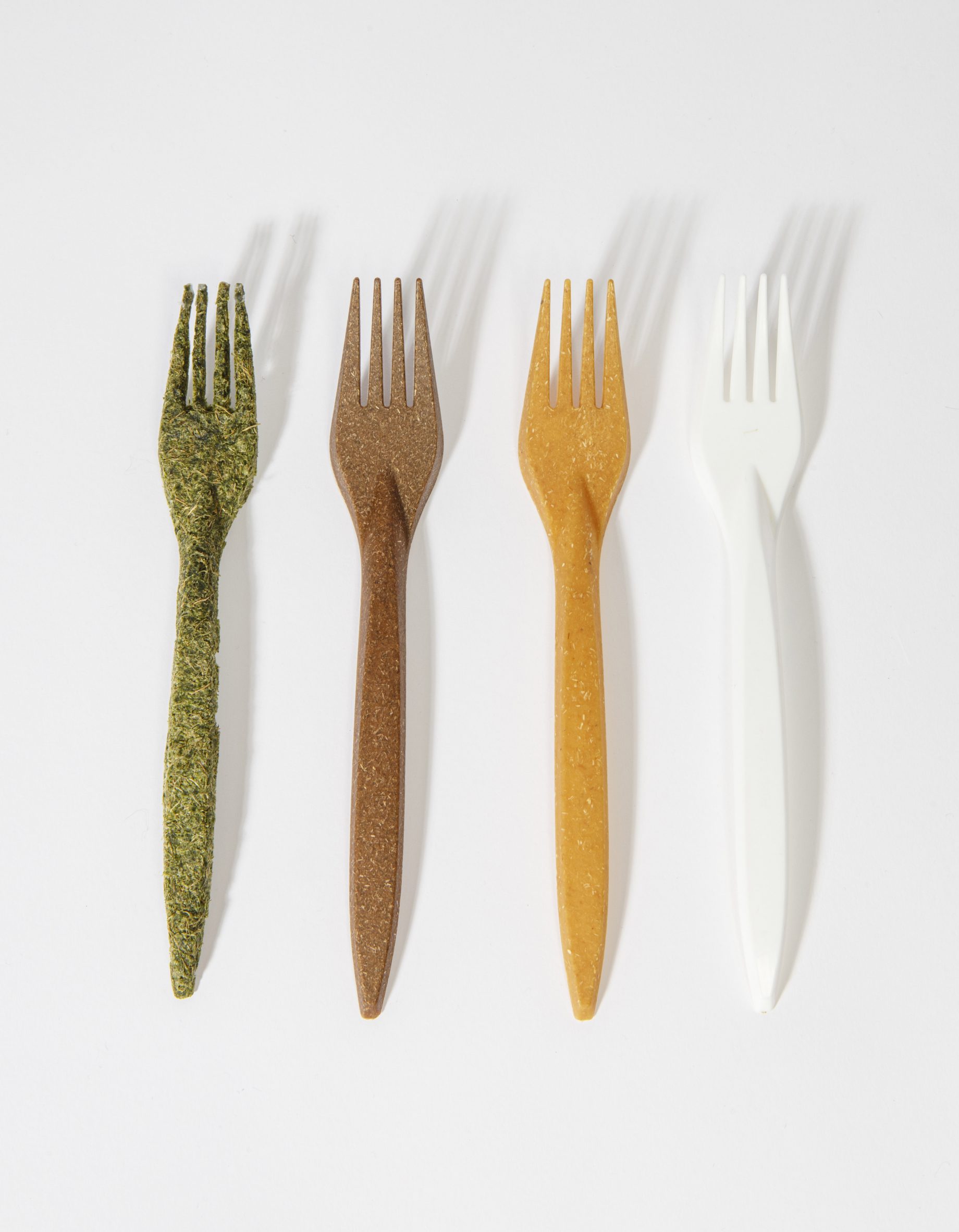 A photograph of four forks made using different natural materials, in tones of green, brown, yellow and white, against a grey background.