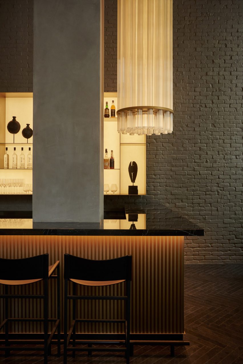 Bar with glossy black counter and ribbed front, above which hangs a tall glass lamp