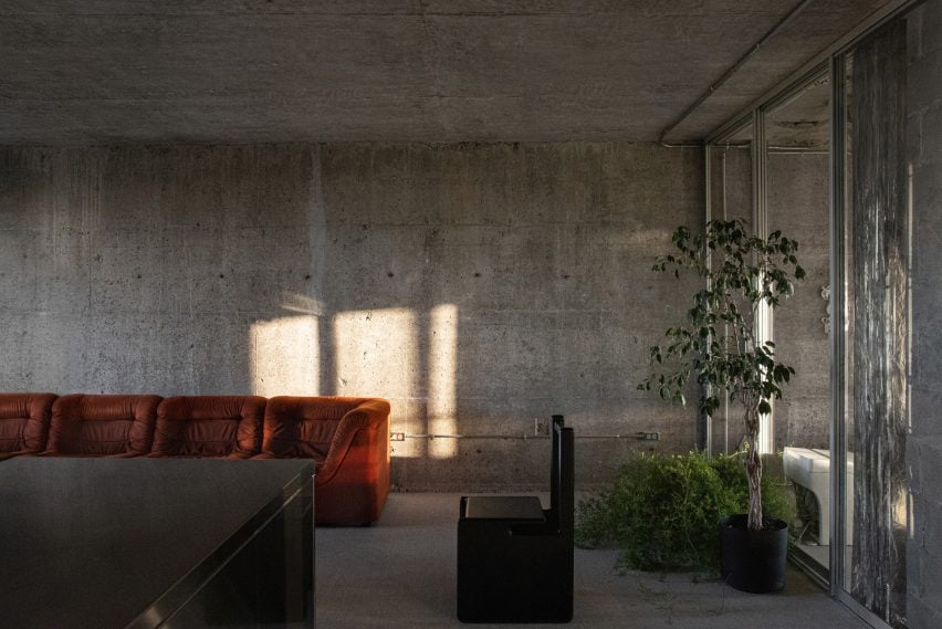 Concrete living room containing a rust-coloured sofa and a black-lacquered chair