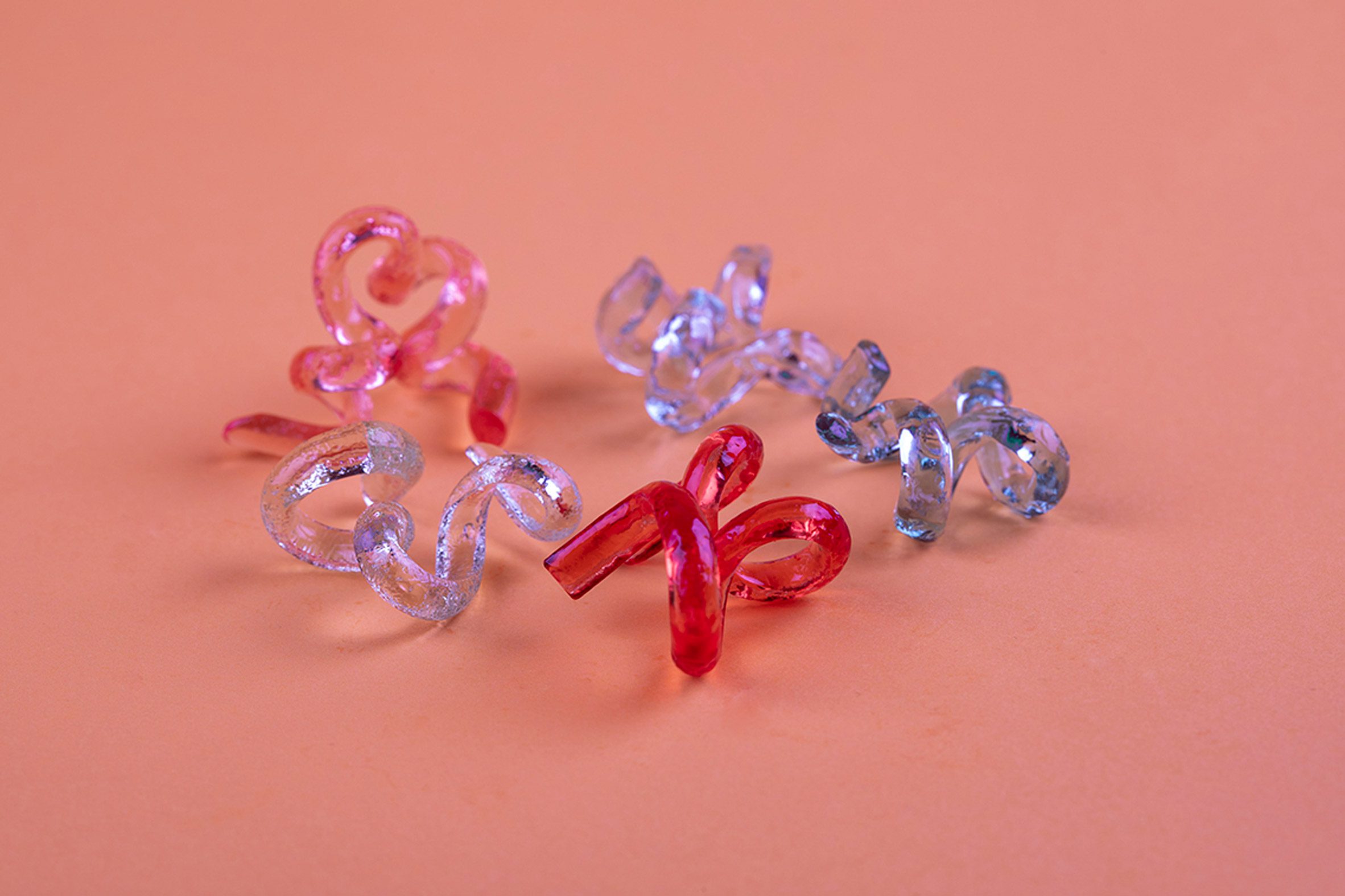 Photo of twisted-up glossy multi-coloured candies by Jinghan Li against a pink background