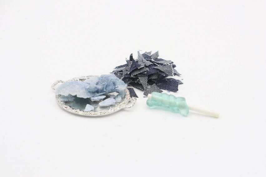 Photo of small scraps of denim fabric, next to a small platter of fabric in the process of being broken down by enzymes, next to a small lollipop-like sweet with light-blue hardened sugar spiralled around a rod by Jinghan Li