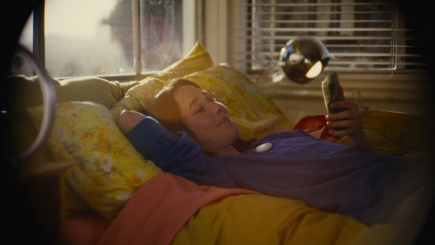 Photo of a young woman wearing the Friend necklace and lying on a bed while playing with her phone