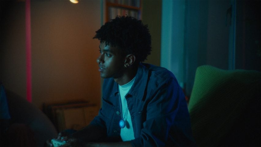 Photo of a young man wearing the Friend necklace around his neck while gaming in a darkened room