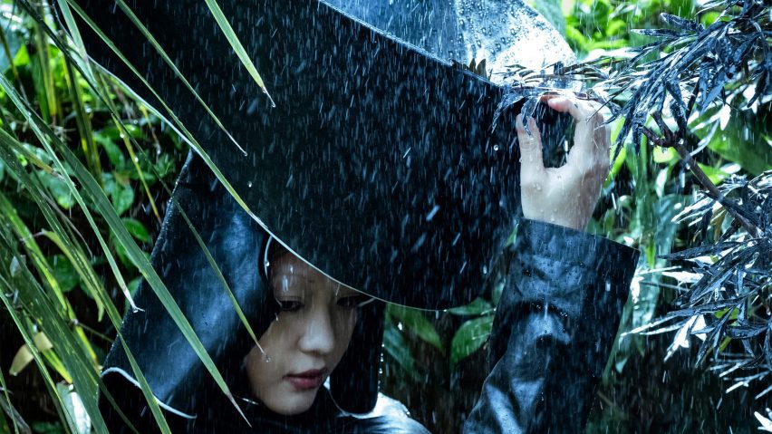 A photograph of a person wearing a large black hat designed to collect rainwater.