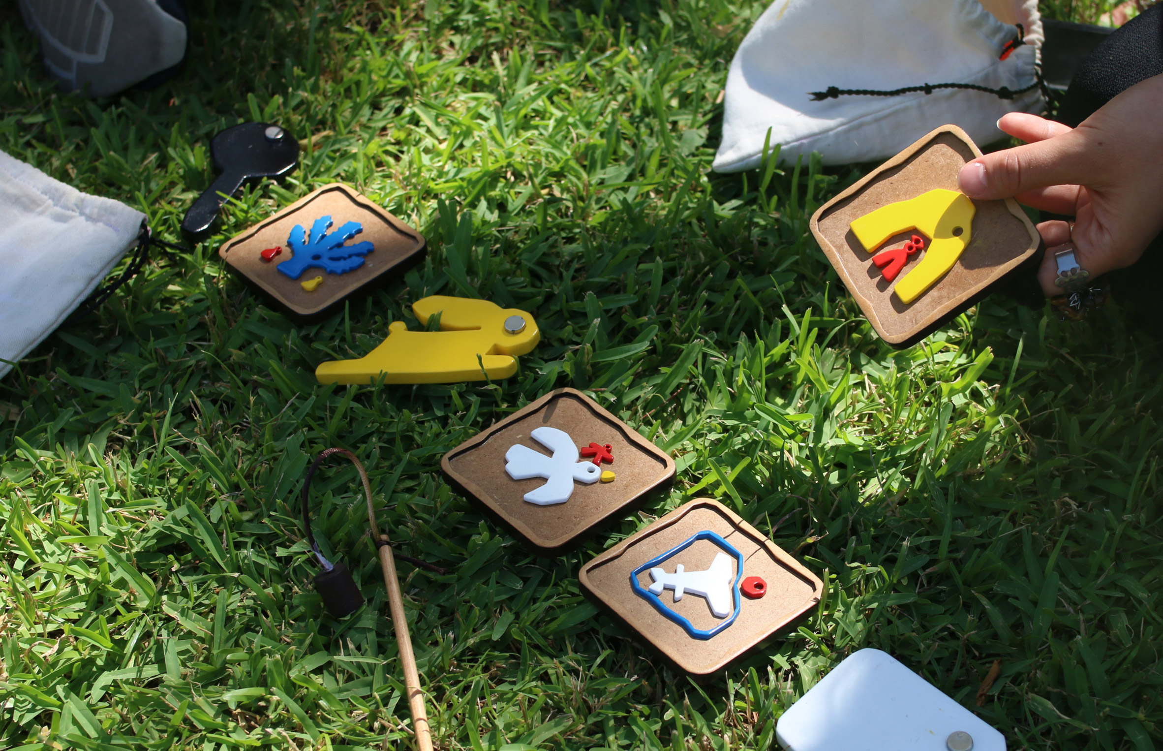 A photograph of a person's hand interacting with wooden squares with various images on them, laid out on green grass.