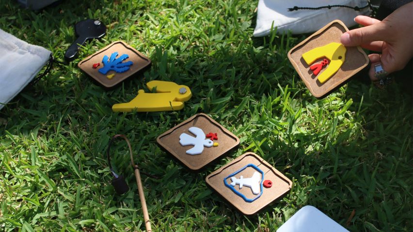 A photograph of a person's hand interacting with wooden squares with various images on them, laid out on green grass.