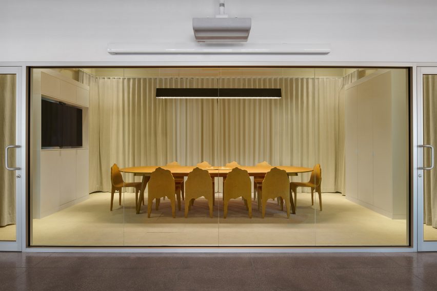 A conference room viewed through a glass wall, featuring wooden furniture