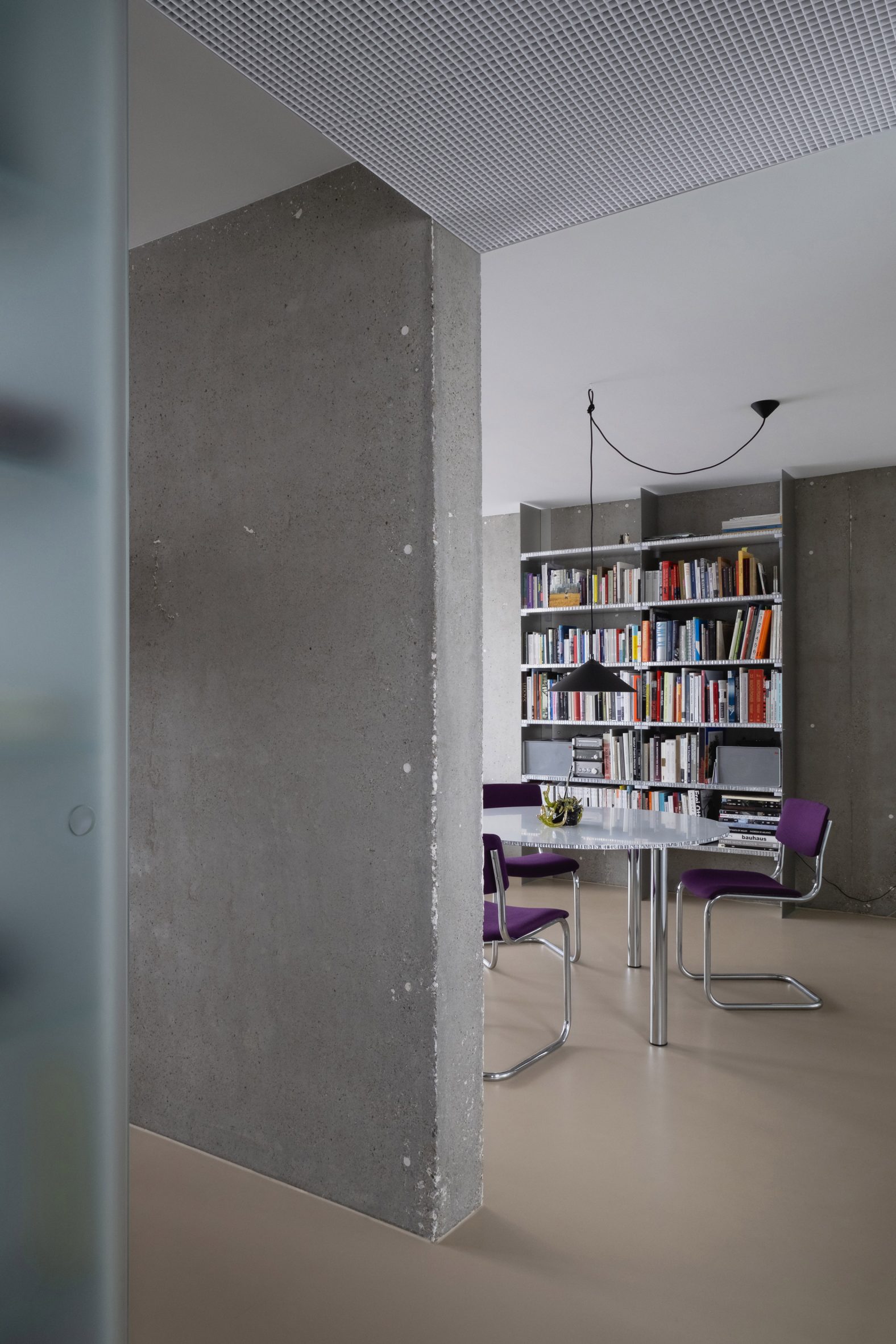 View past concrete wall into living area with metallic dining set