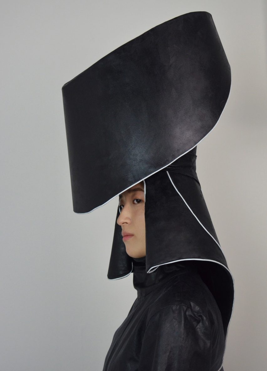 A photograph of a person from the side wearing a large black headpiece which is designed to collect rainwater.