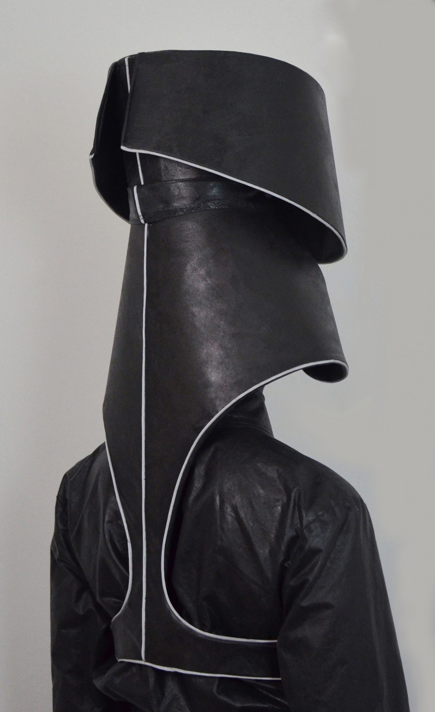 A photograph of a person from behind wearing a large black headpiece which is designed to collect rainwater.