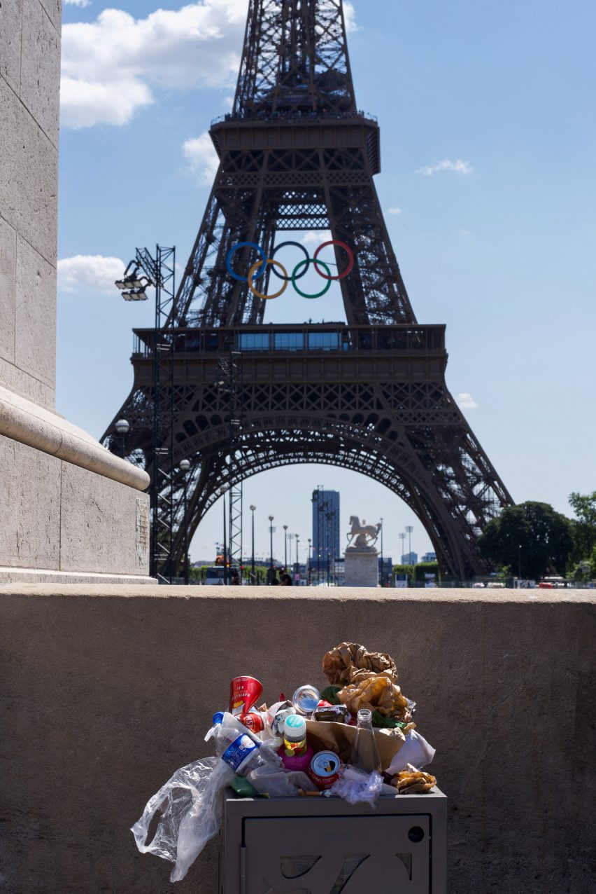 An overflowing rubbish bin with the Eiffel Tower in the background bearing the Olympic rings