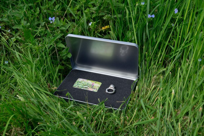 Close-up photo of a metal case containing a ring and a small map, lying on the grass