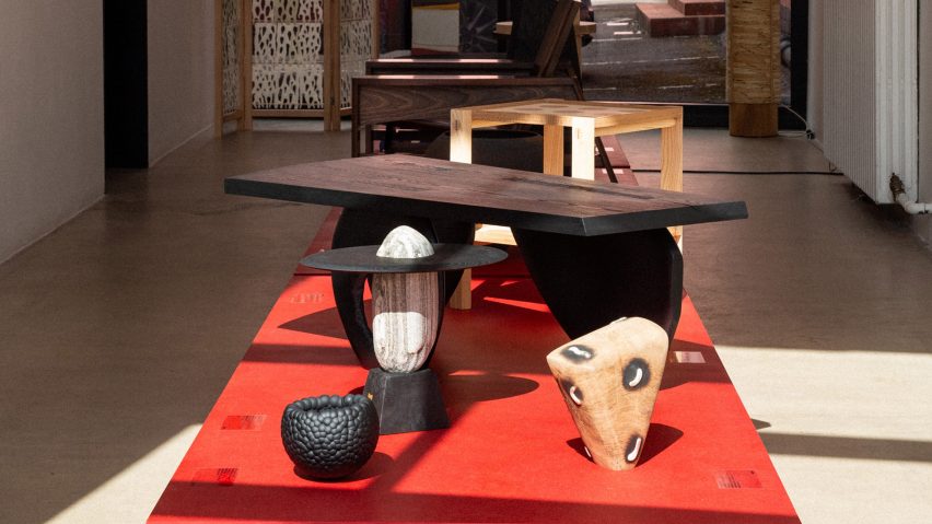 A photograph of sculptures and wooden furniture in an exhibition, displayed on a red plinth.