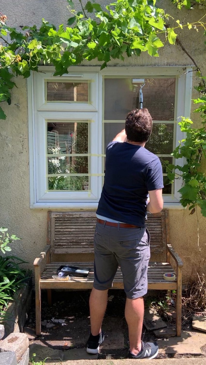 Video still of a man painting the outside of the windows on a house with a translucent, paint-like substance