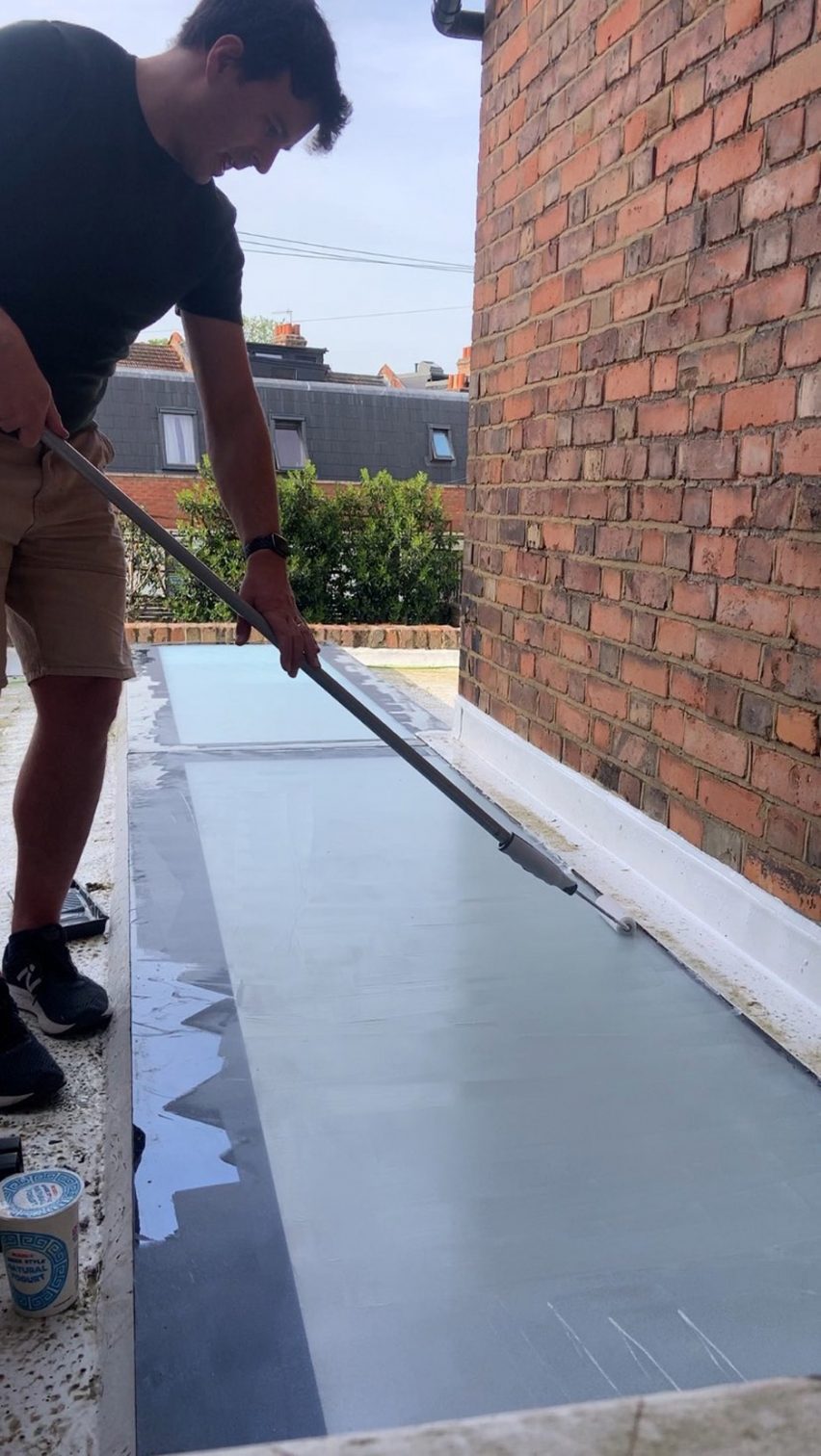 Photo of a man painting a translucent creamy substance on a sheet of glass laid on the ground with a roller