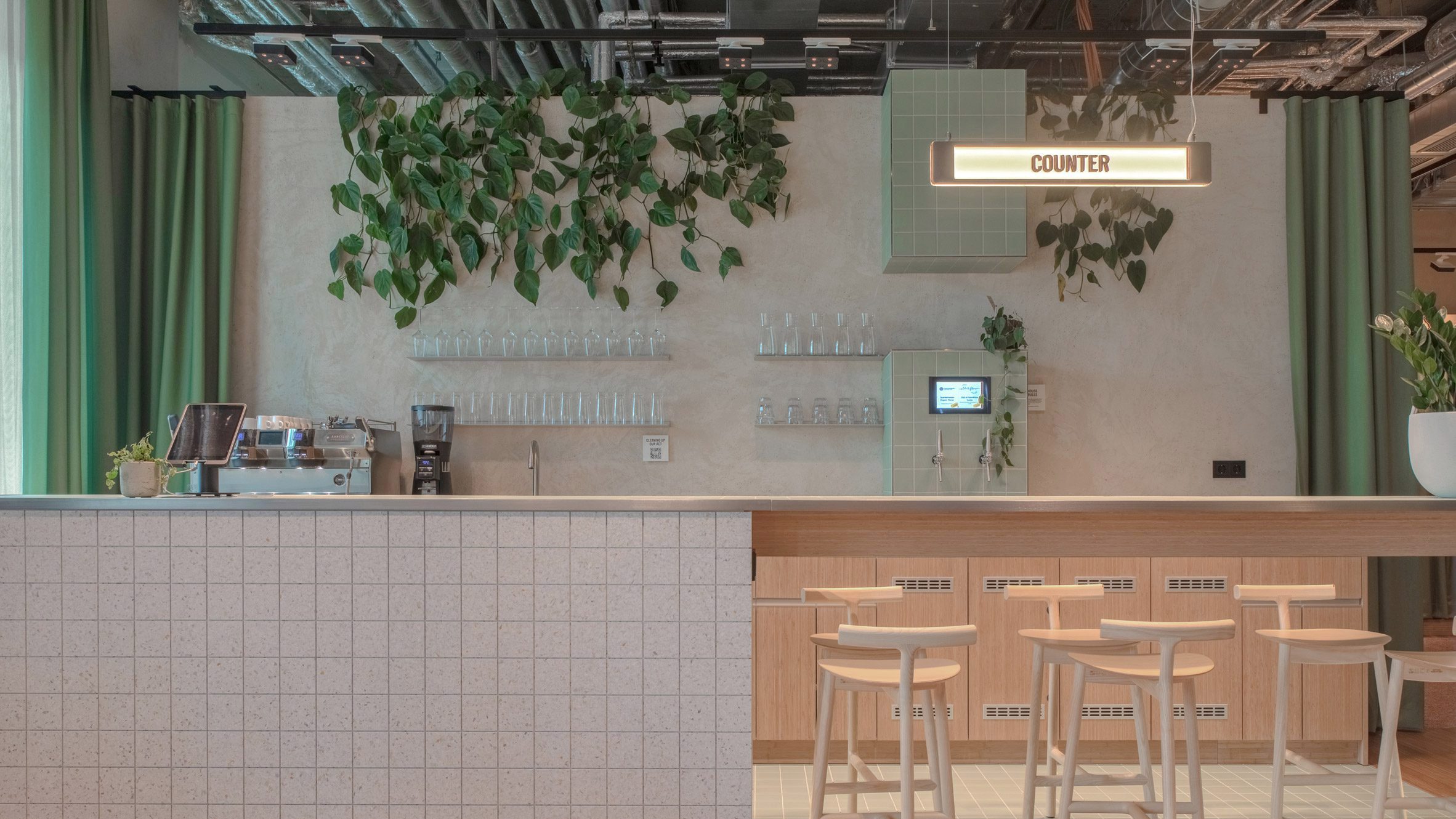 Photograph of the hotel self-serve bar with wooden bar stools and fake foliage hanging from the ceiling.