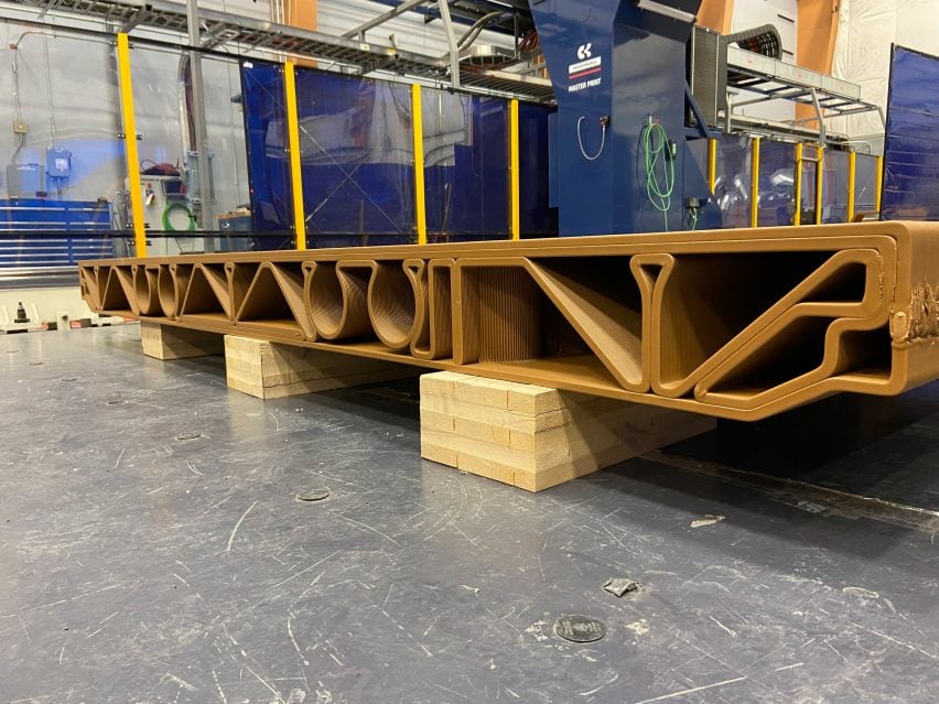 Photo of a large 3D-printed, wood-coloured structure with a flat top surface and elaborate geometry of channels and paths running through its cross-section