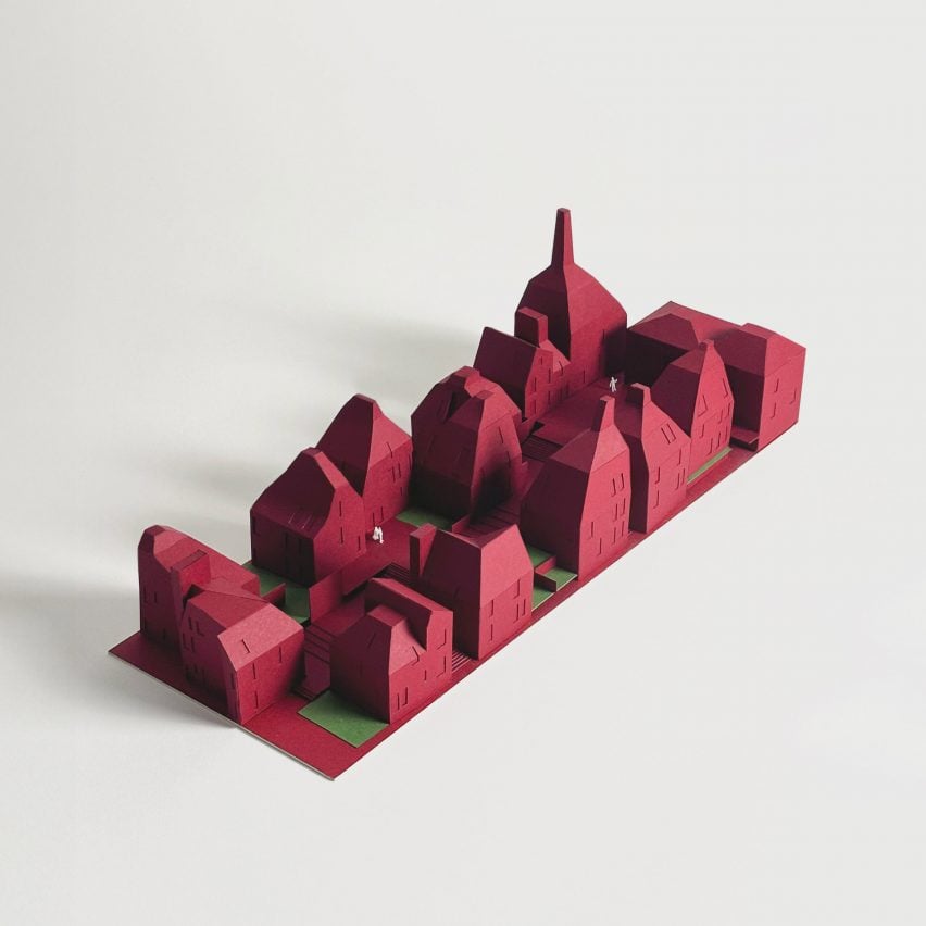 A photograph of a red architectural model of a housing complex, against a white background.