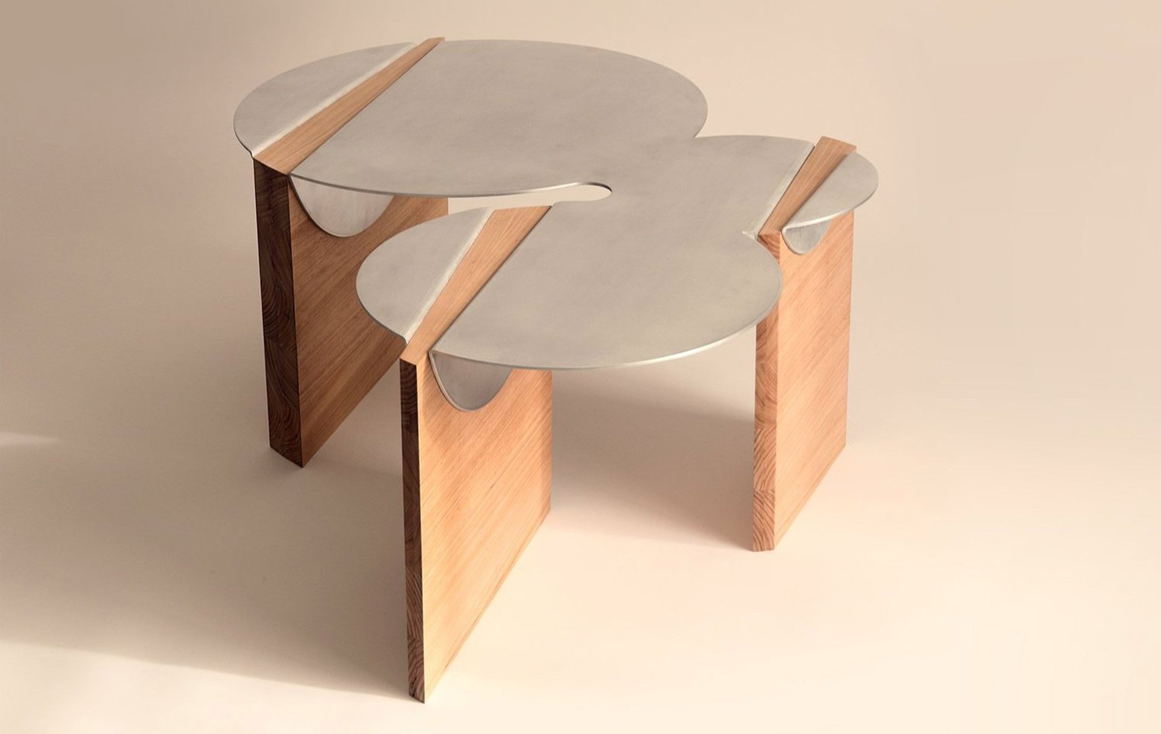 A photograph of a table, with a silver tabletop in abstract circular shapes atop three brown wooden legs.