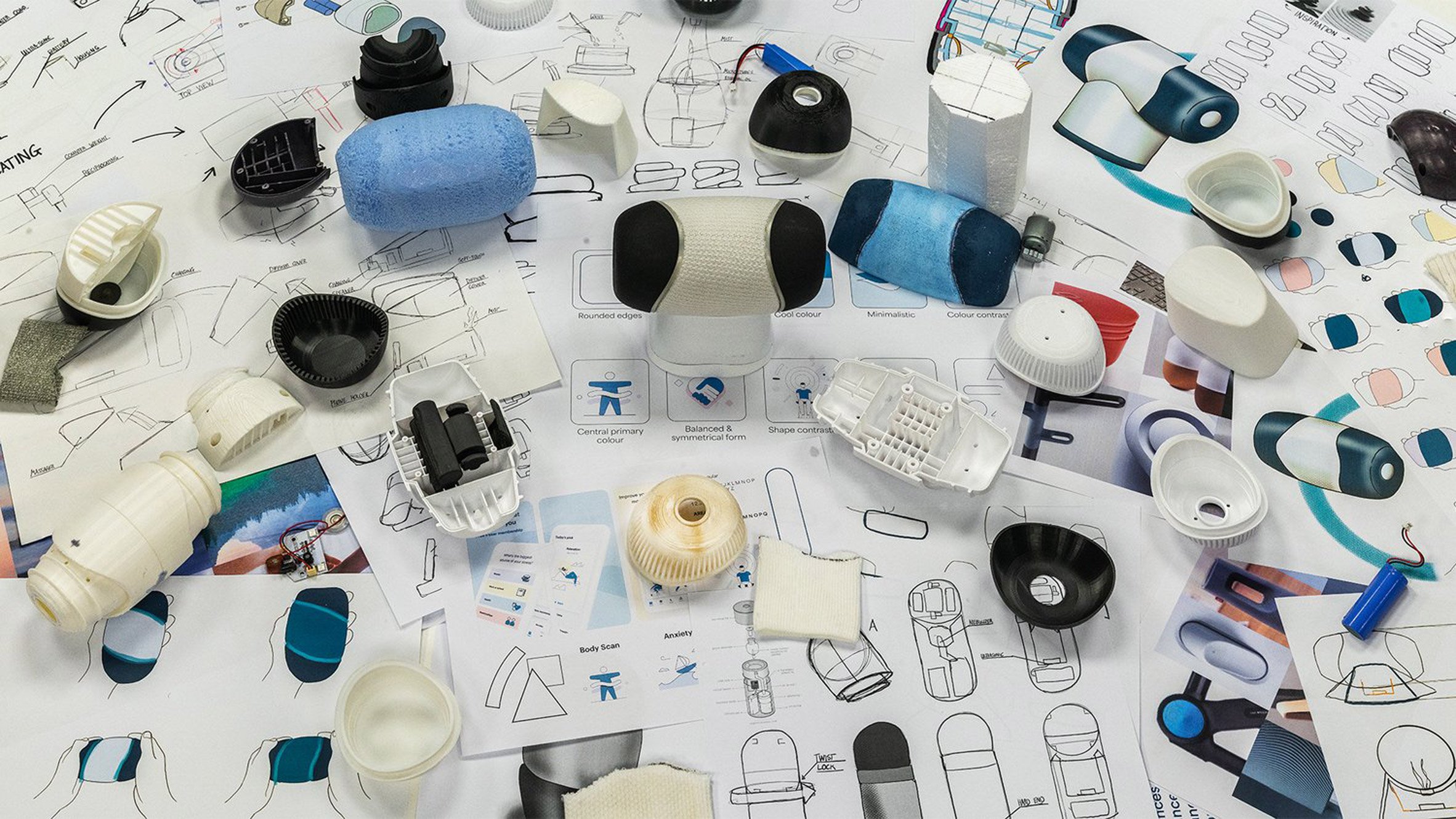 A photograph of various prototypes and sketches for a massage device, in tones of blue, white and black.